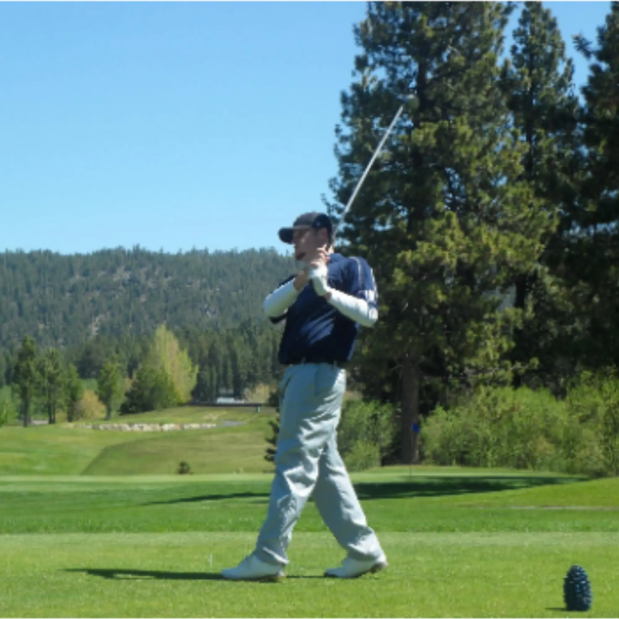 Golfer in follow-through after a tee shot with mountains in the background