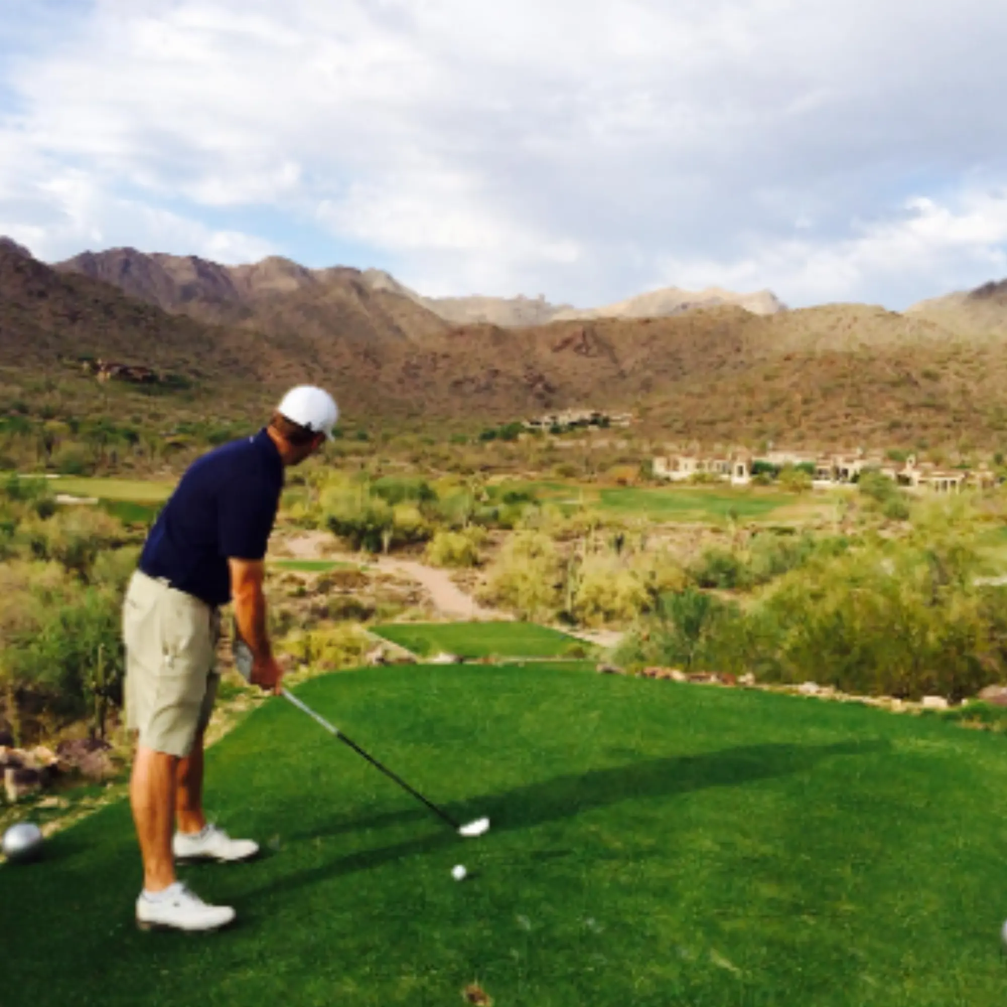 Golfer addressing the ball at a desert tee with mountains beyond