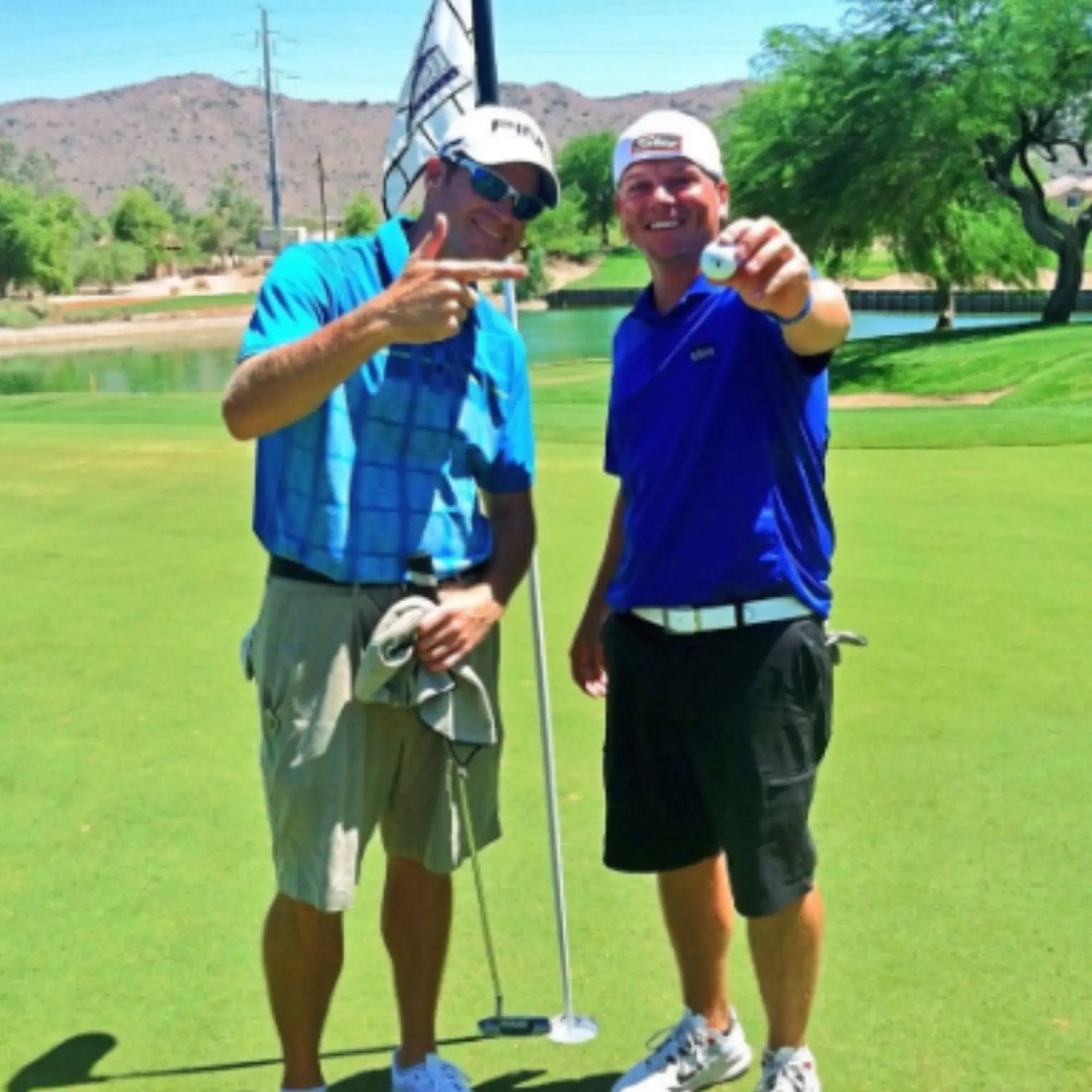 Two golfers celebrating with a ball held up at the pin