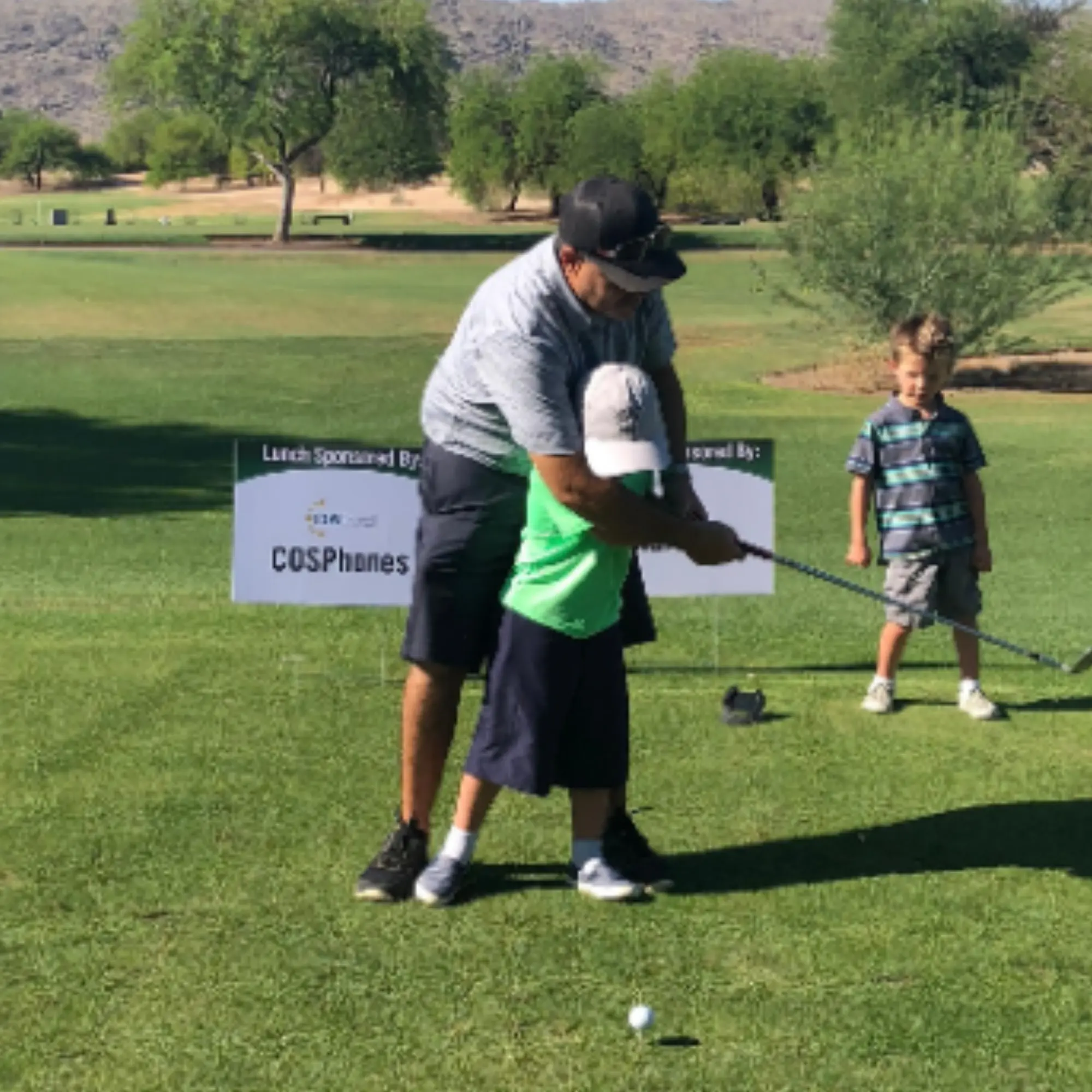 Adult coaching a child through a swing on the tee box